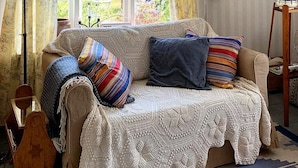 Een gezellige woonkamer met een beige bank, een gebreide plaid en kleurrijke kussens.