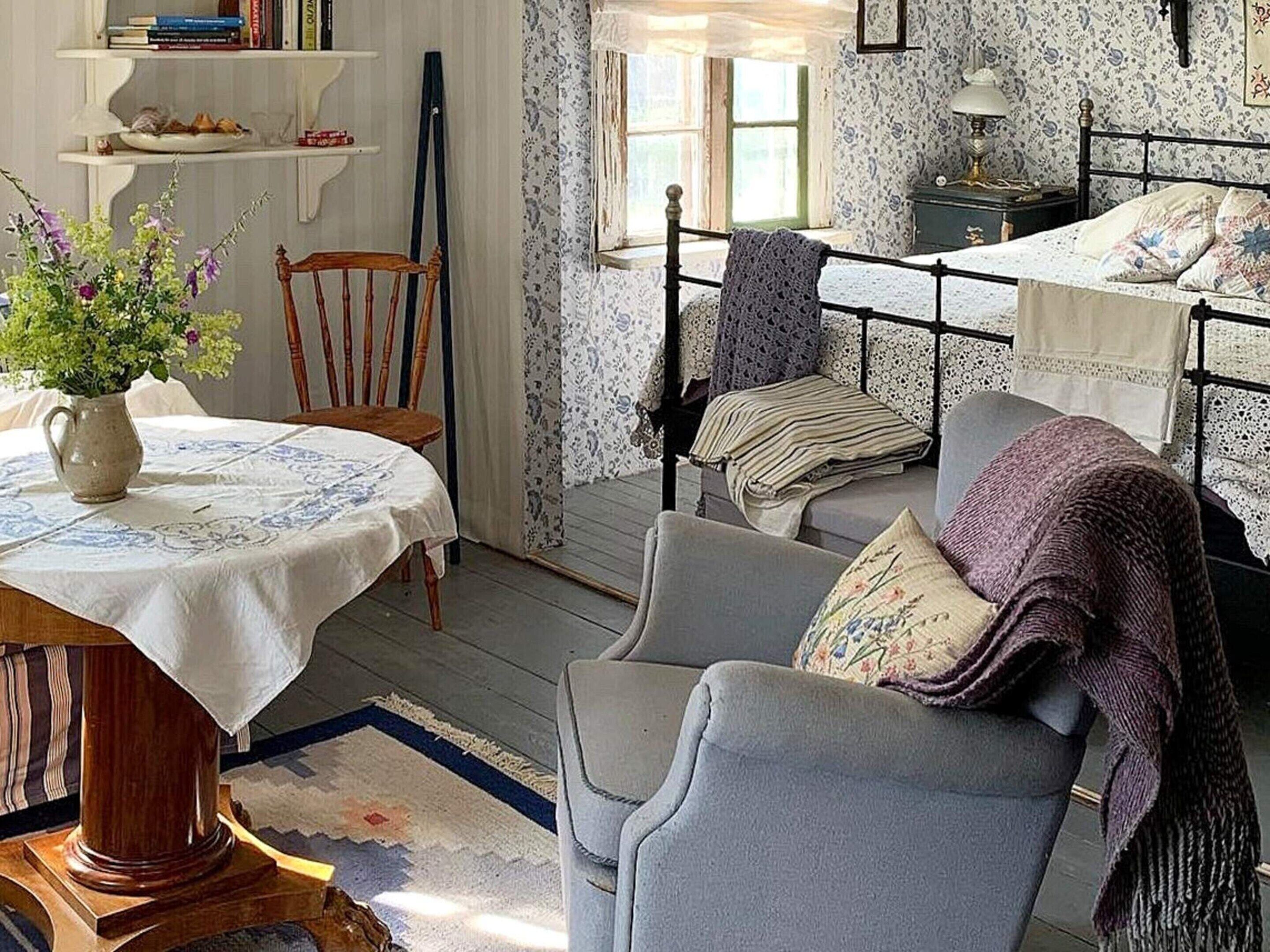 A cozy bedroom with a bed, a chair, a table with a vase of flowers, and a bookshelf.