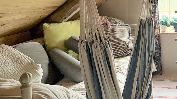 Een hangmatbed in een kamer in loft-stijl met een schuine plafond, kussens en een raam met planten.