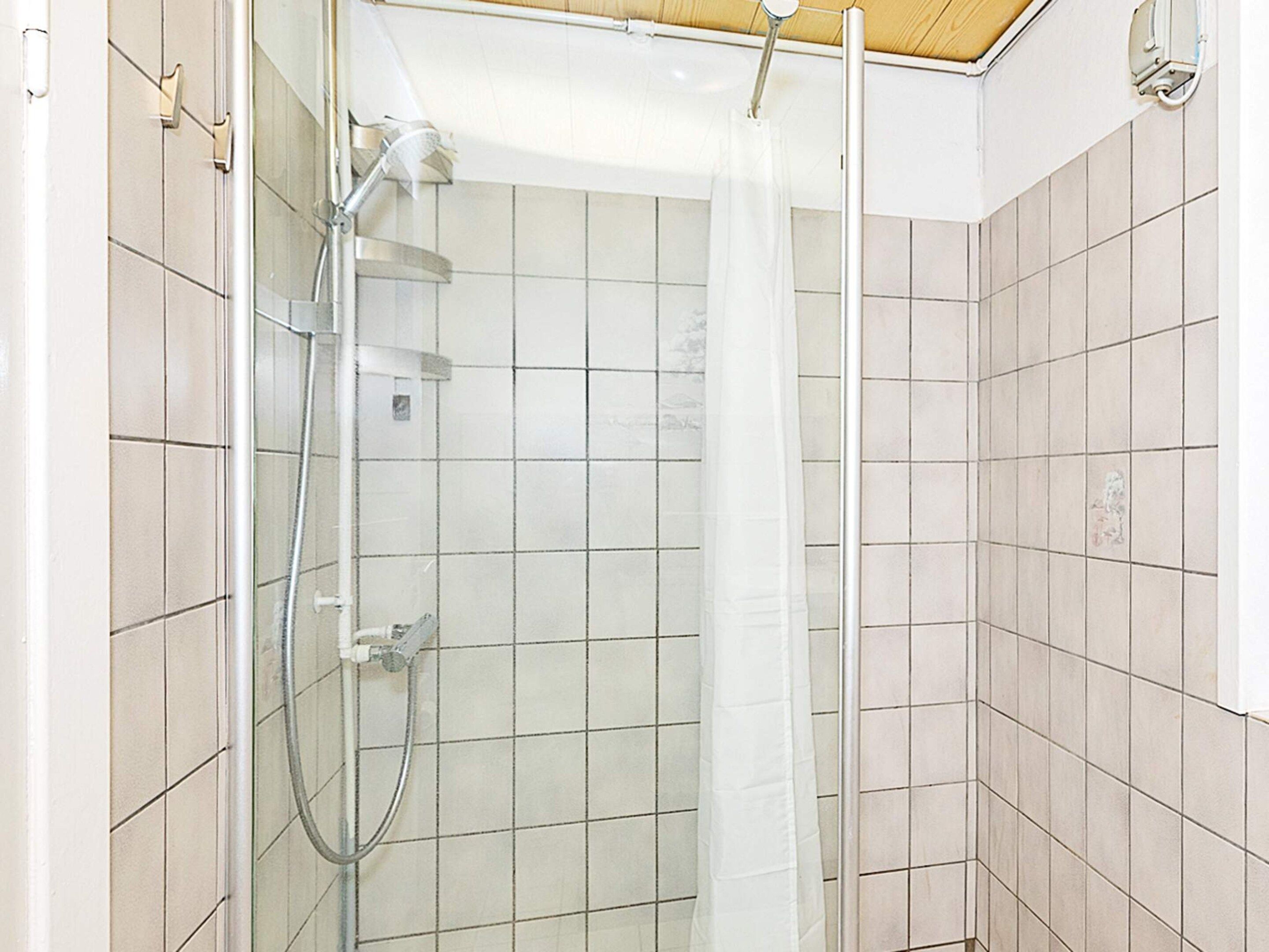 A shower with a glass door, a handheld showerhead, and a vertical water stream.