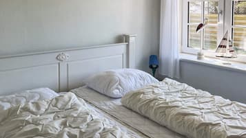 A bedroom with two beds, a window with curtains, and a nightstand with a lamp.