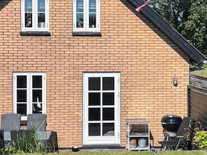 A brick house with two windows, a door, and outdoor furniture including chairs and a grill. - 4 Person Holiday Home in Hanstholm (Hanstholm)