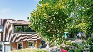 A two-story house with a sloped roof, a brick exterior, and a garden with various plants and a red bench. - 4 Person Holiday Home in Hanstholm (Hanstholm)