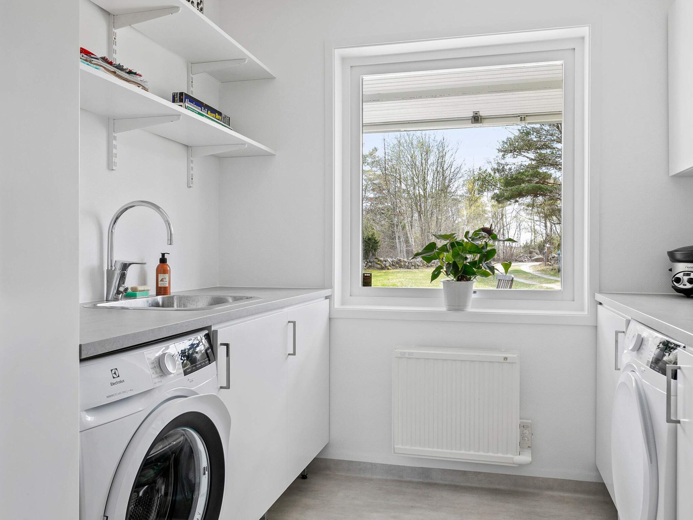 Une cuisine moderne équipée d’un lave-linge intégré, d’une fenêtre donnant sur les arbres et d’un radiateur.