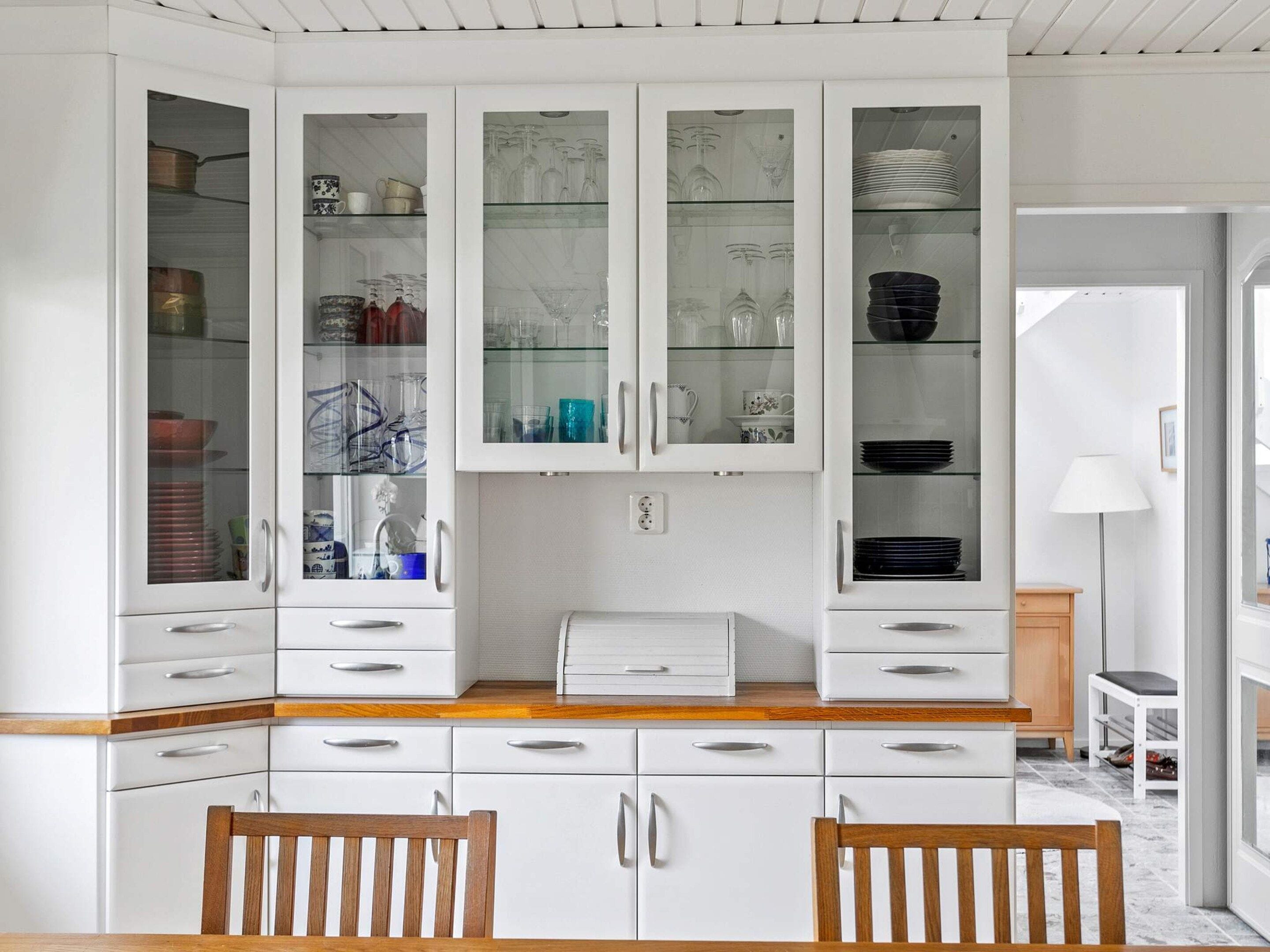A kitchen with white cabinets, a wooden countertop, and a dining area with two wooden chairs.