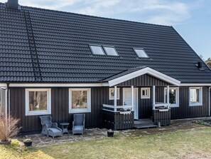 Una casa moderna con techo oscuro, detalles blancos y un porche con dos sillas y una mesa.