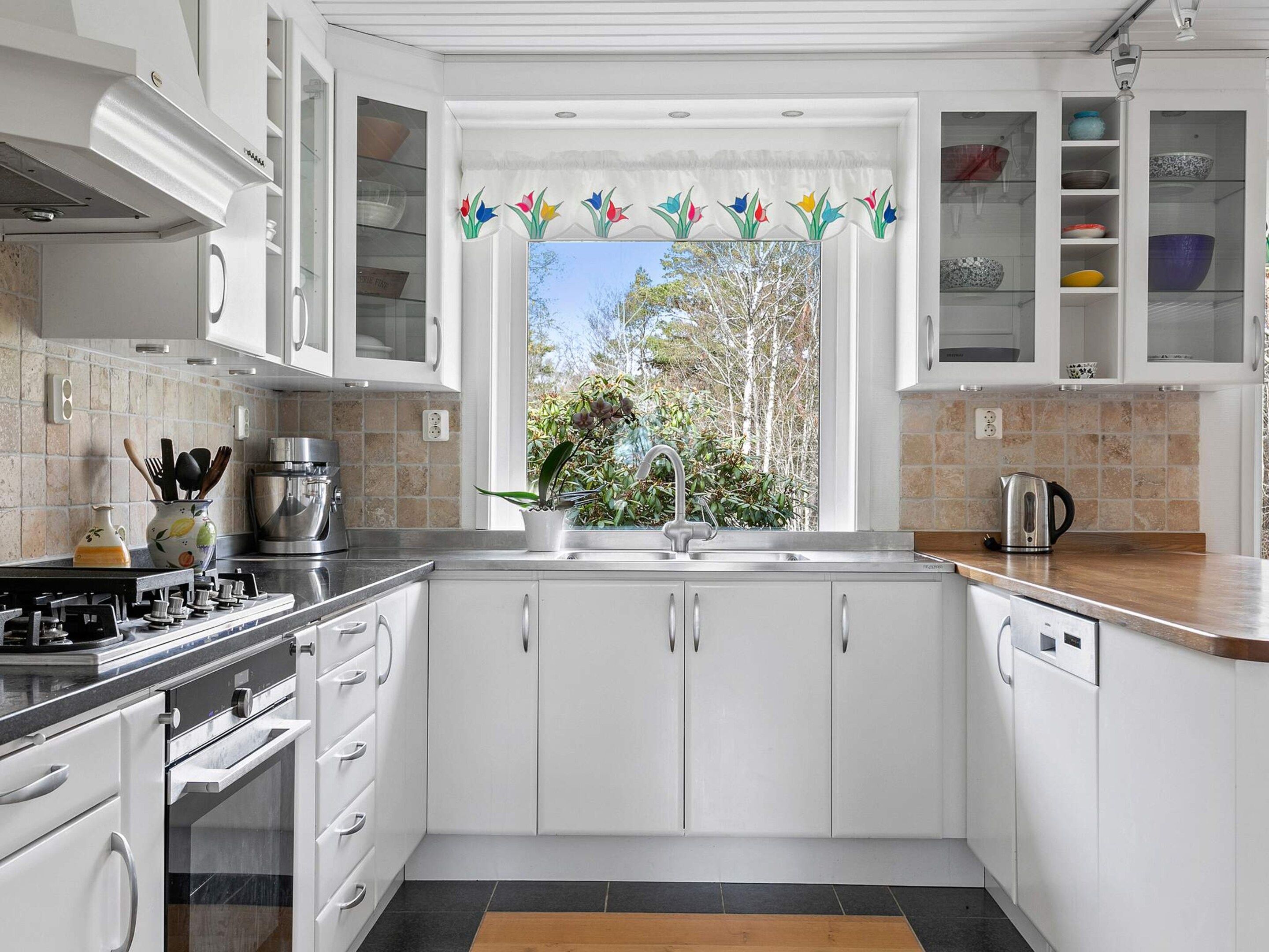 A modern kitchen with white cabinets, a stainless steel range, and a window with a view of trees.