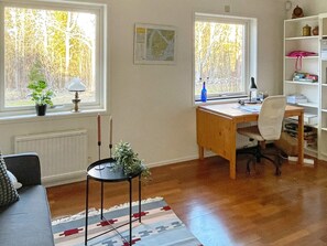 Una habitación con un escritorio de madera, una silla, una estantería, un radiador y una ventana con vistas a árboles.