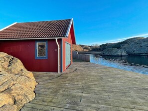 A red building with a tiled roof, a wooden dock, and a calm body of water. - 4 Star Holiday Home in Nosund (Nosund)