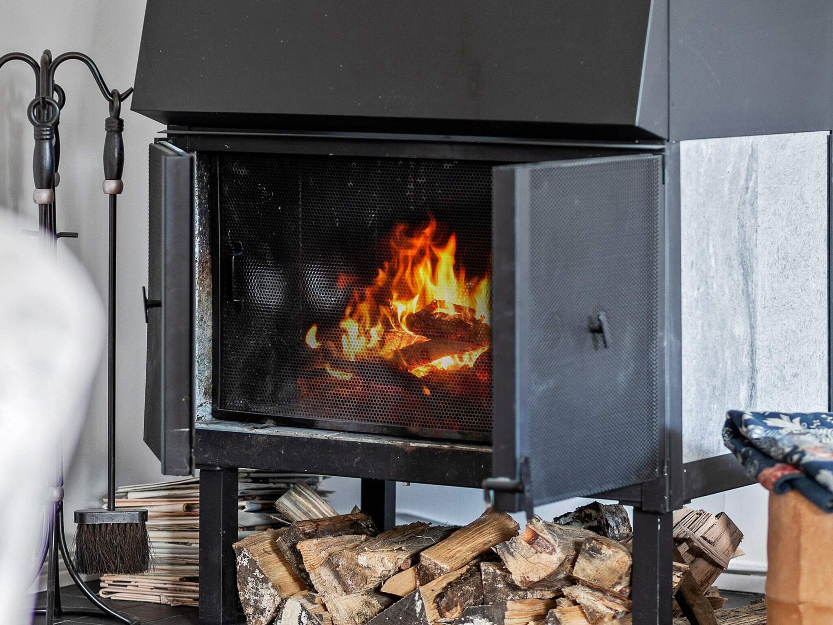A wood-burning stove with visible flames, a metal grate, and a stack of firewood.