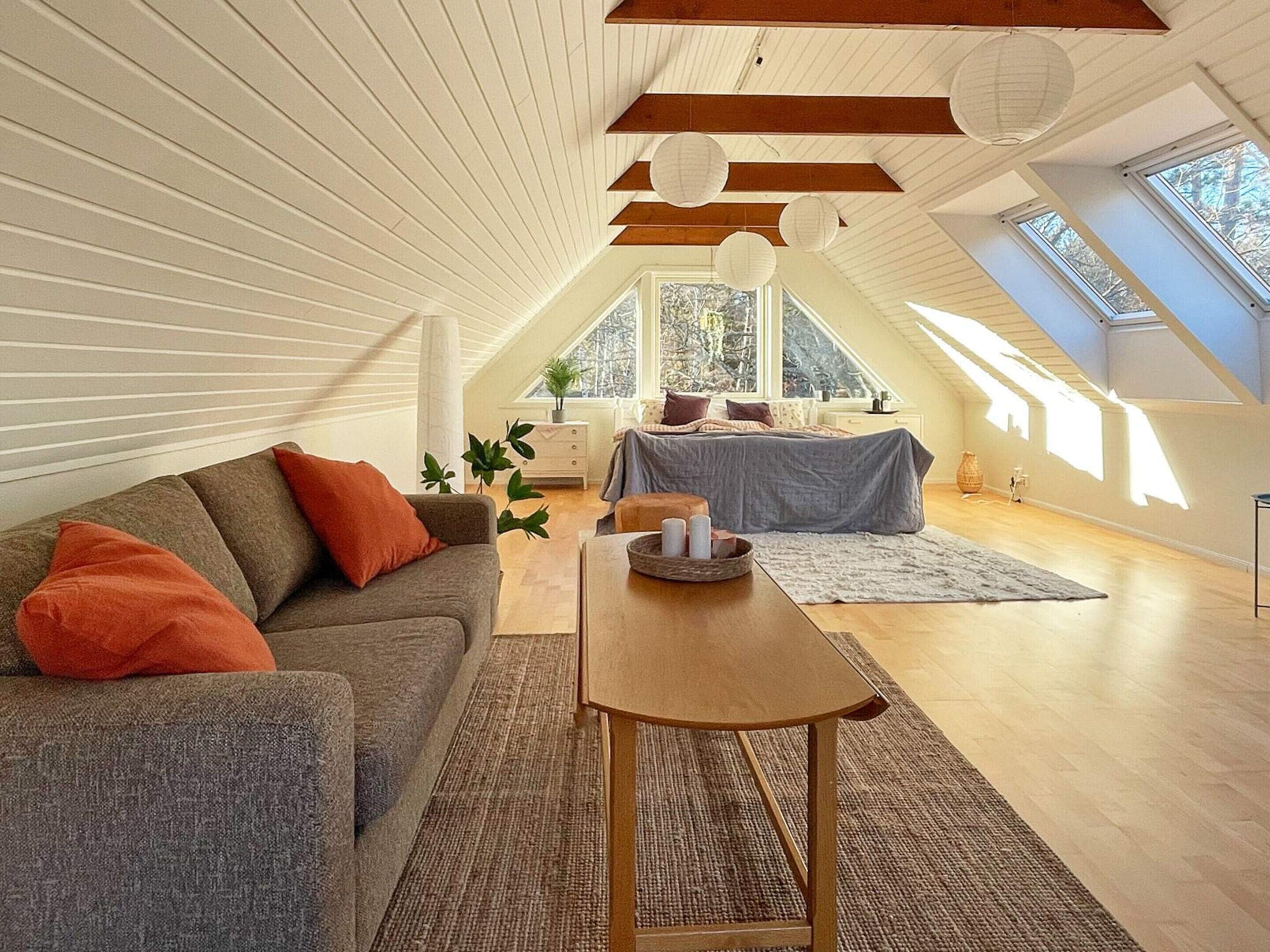 Ein geräumiges Schlafzimmer im Loft-Stil mit schrägen Wänden, einem großen Fenster und einer gemütlichen Sitzecke mit Sofa und Tisch.