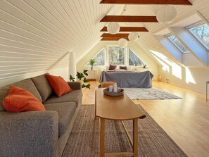 Un espacioso dormitorio tipo loft con techo inclinado, un ventanal grande y una zona de estar acogedora con sofá y mesa.