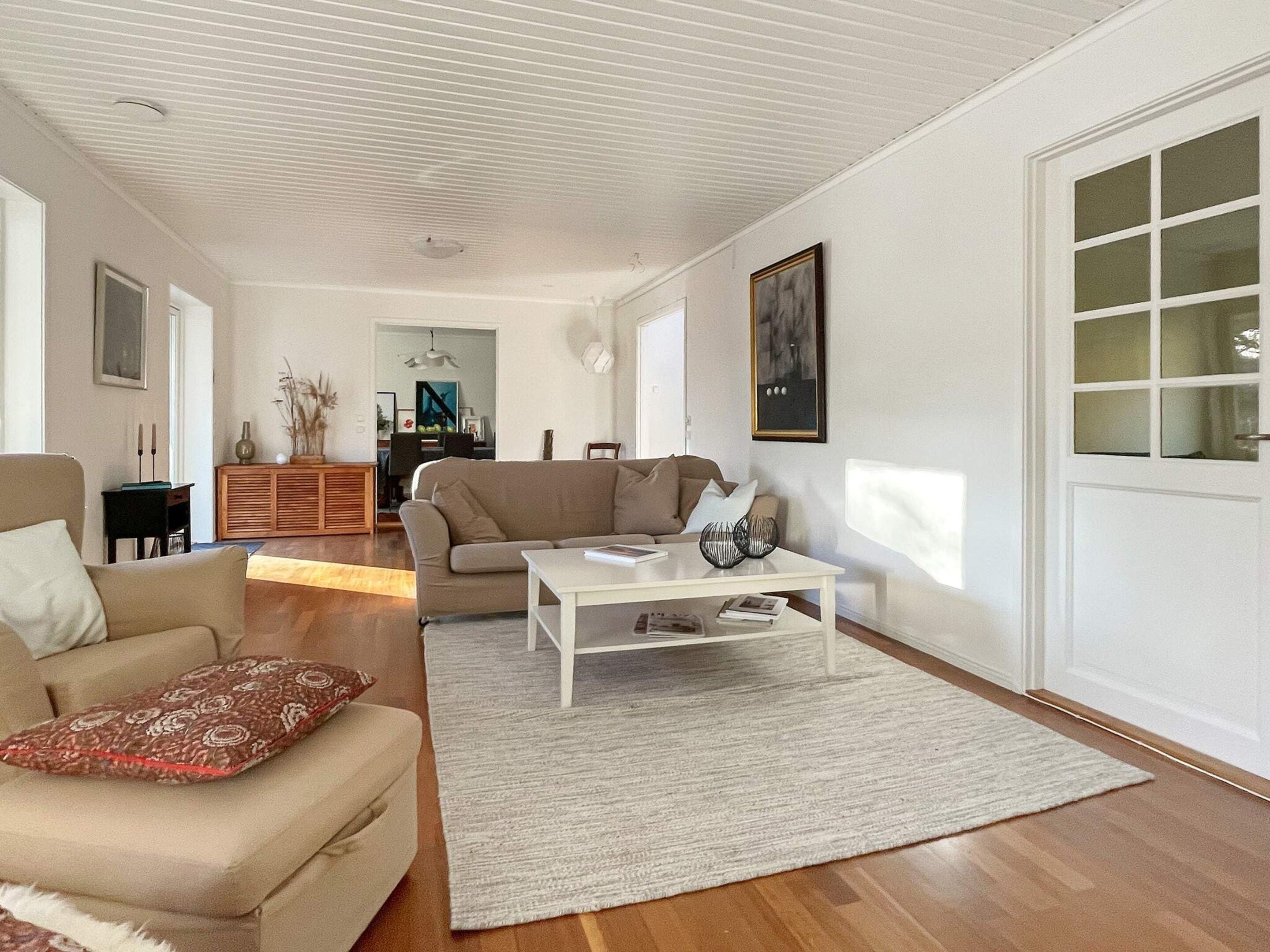 A living room with a sofa, a coffee table, and a dining area in the background.