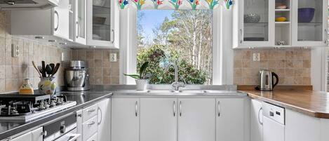 A modern kitchen with white cabinets, a stainless steel range, and a window with a view of trees.