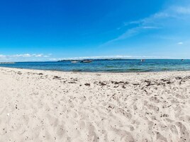 A beach with clear blue water, boats, and distant land.