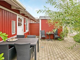 En rød bygning med en fliseterasse, udendørs siddepladser og et træ.