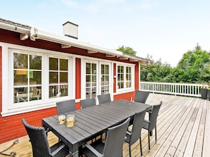 A deck with a table and chairs, a white railing, and a red building with large windows. - 6 Person Holiday Home in Aabenraa (Aabenraa)