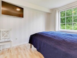 A bedroom with a bed, a chair, a window, and a wall-mounted TV.
