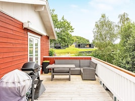 A deck with outdoor furniture, a grill, and a view of a house and landscape.