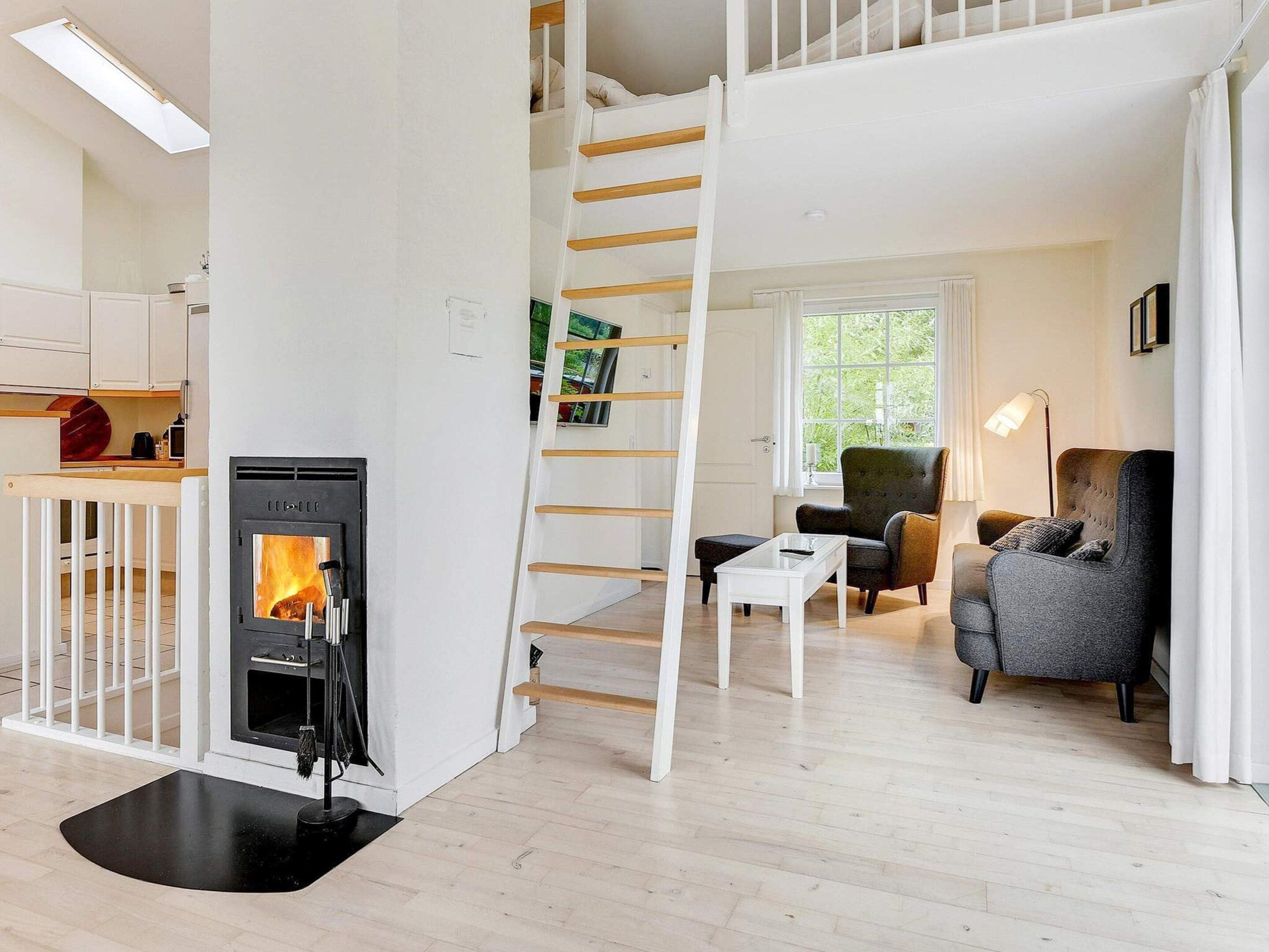 A modern interior with a fireplace, a wooden staircase, and a seating area with a sofa and armchairs.