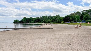 Uma praia com areal, um cais e uma área arborizada ao fundo.
