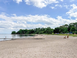 Una playa con arena, un muelle y un área boscosa al fondo.
