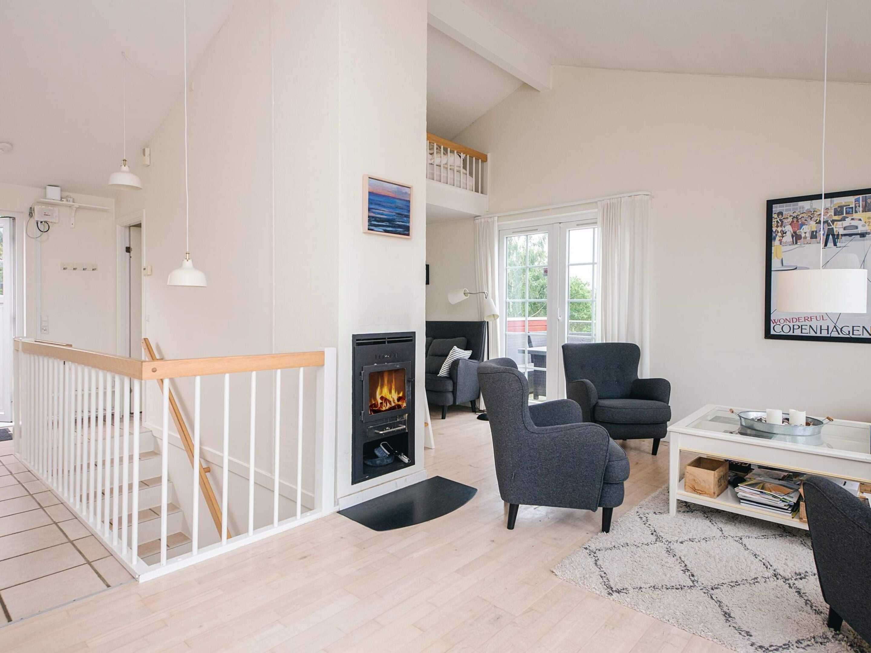 A modern living room with a fireplace, a staircase, and a seating area with armchairs.