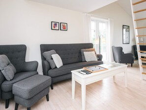 A modern living room with a grey sofa, matching armchair, and a coffee table. There are two framed pictures on the wall, a window with curtains, and a wooden ladder. - 6 Person Holiday Home in Aabenraa (Aabenraa)