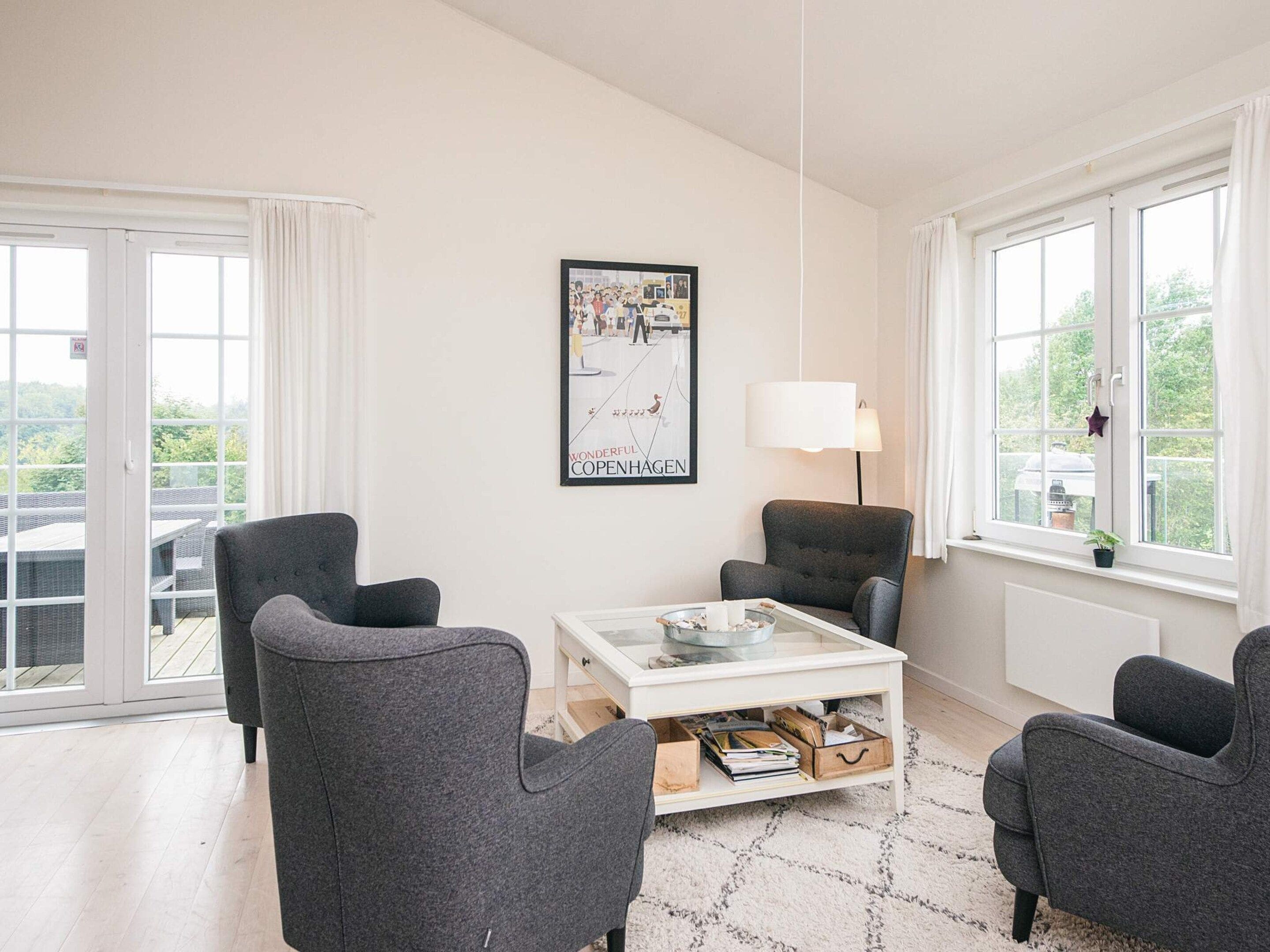 A modern living room with a glass coffee table, grey armchairs, a white lamp, and a framed picture on the wall.