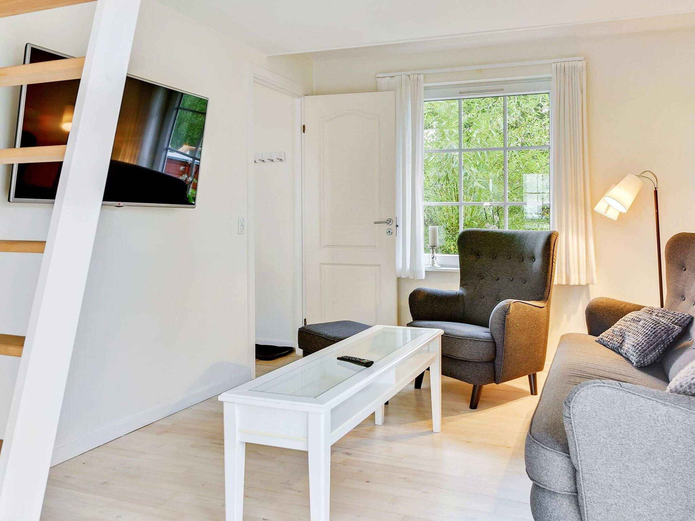 Una sala de estar moderna con televisor, sofá, sillón y ventana con vista a follaje.