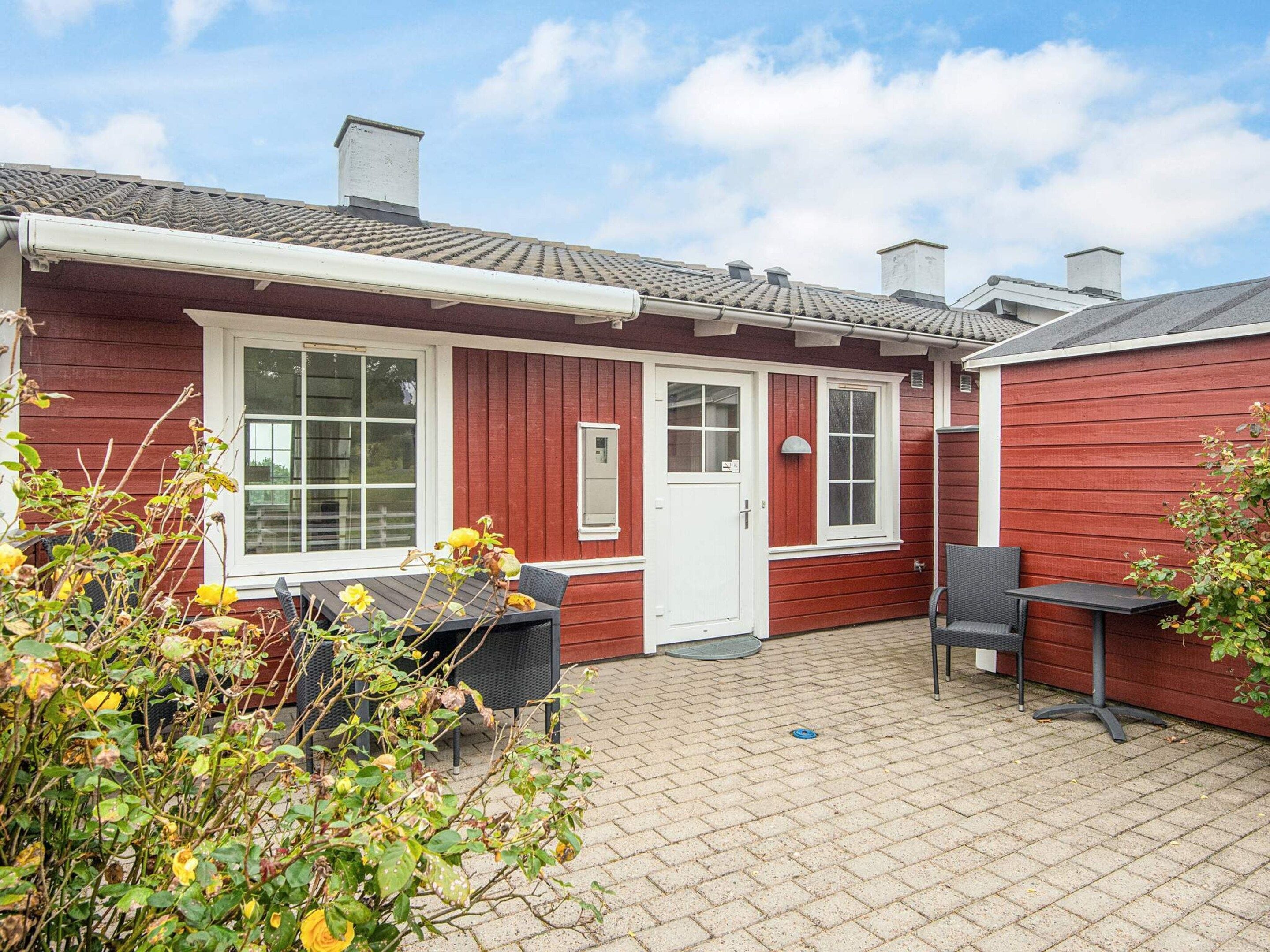 A red building with a white door, a window, and a small outdoor seating area with a table and chairs.