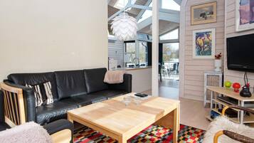 A modern living room with a black leather sofa, a wooden coffee table, and a colorful rug.