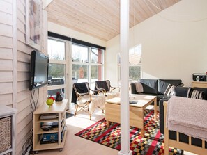 En moderne stue med et tv ophængt på væggen, en sofa, to lænestole, et sofabord og en tæppe med et mønster.