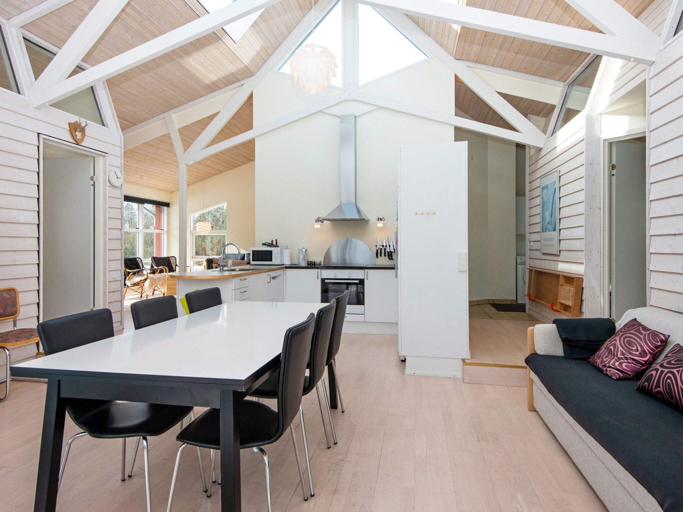 Een moderne keuken met witte kastjes, een magnetron en een fornuis. Er is een eethoek met een tafel en stoelen.