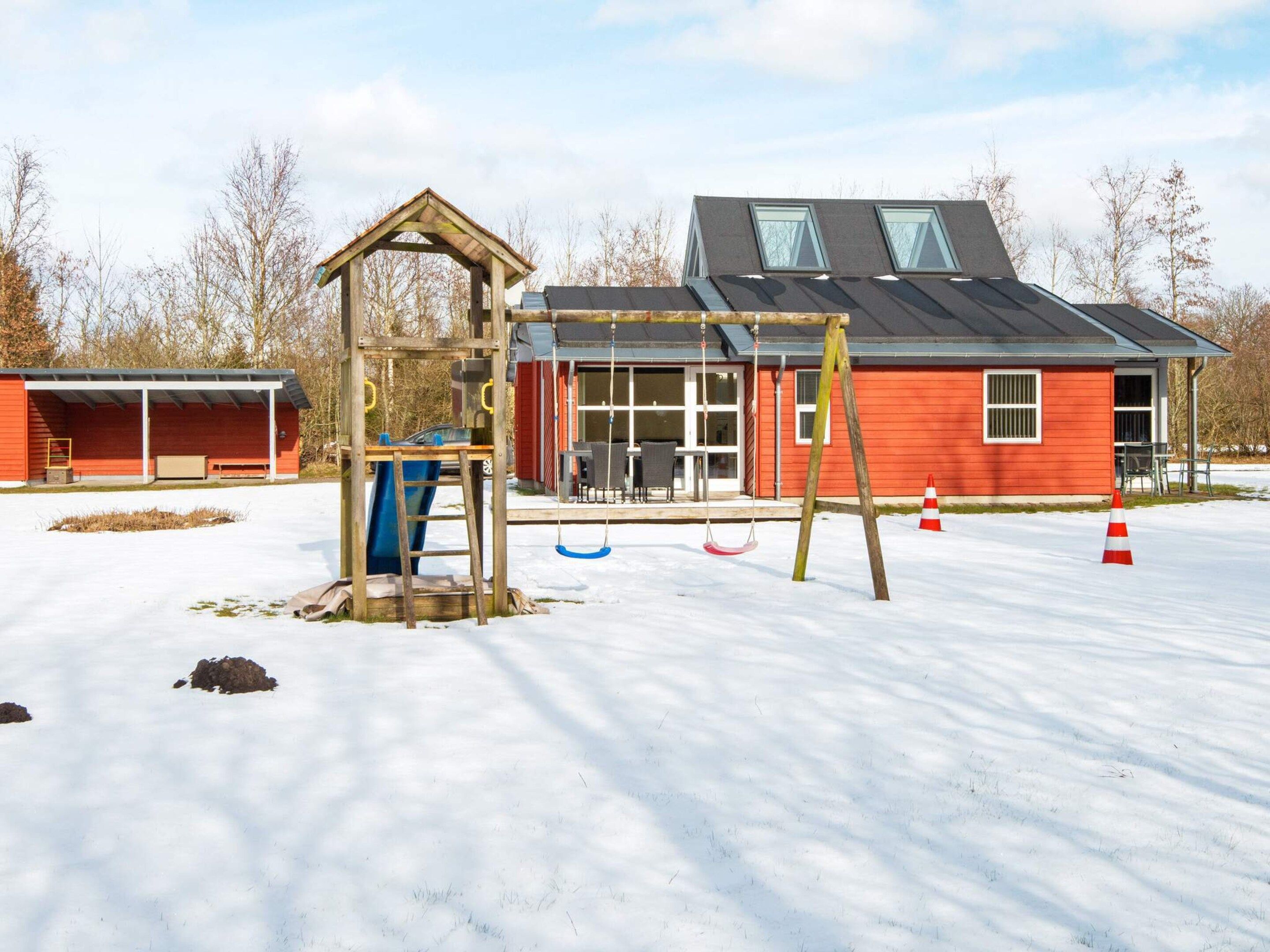 A playground with swings and a climbing structure, a red building with a covered area, and a snow-covered ground.