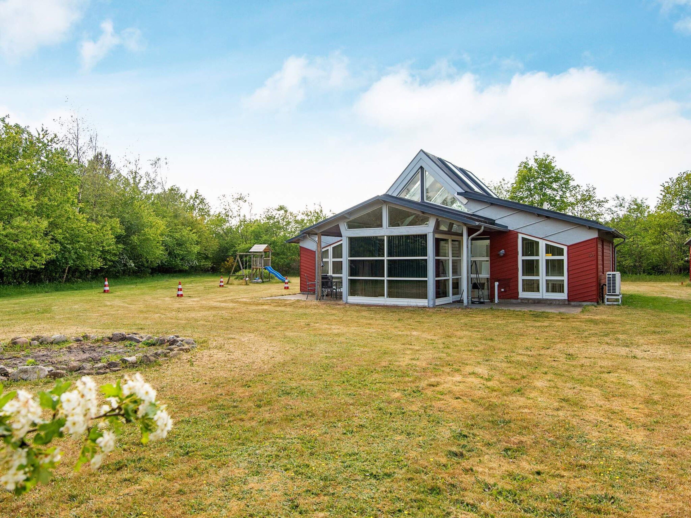 A two-story building with large windows and a sloped roof, surrounded by a grassy yard and trees.