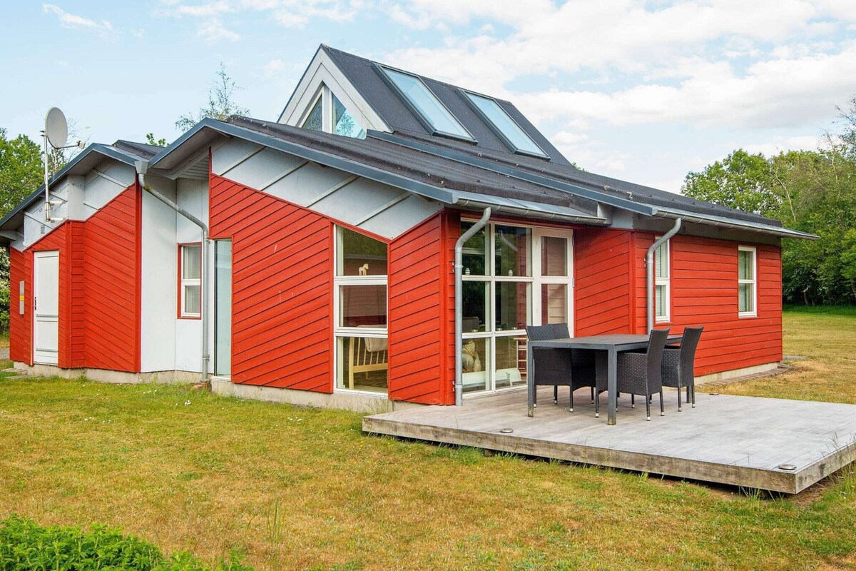 A red building with a sloped roof, large windows, and a patio area with a table and chairs.