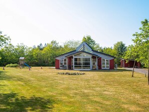 Um edifício vermelho com uma grande janela de vidro, um campo gramado e um parquinho com um escorrega.