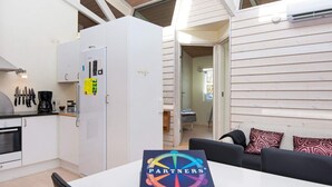 A modern kitchen with white cabinets, a refrigerator, and a coffee maker. There is a dining table with a box labeled 'PARTNERS+'.