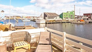 Un port de plaisance avec des bateaux amarrés, une terrasse en bois avec des sièges et des bâtiments en arrière-plan.