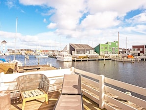 Un port de plaisance avec des bateaux amarrés, une terrasse en bois avec des sièges et des bâtiments en arrière-plan.