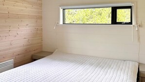 Una cama individual con colchón acolchado en habitación con paredes de madera y ventana.