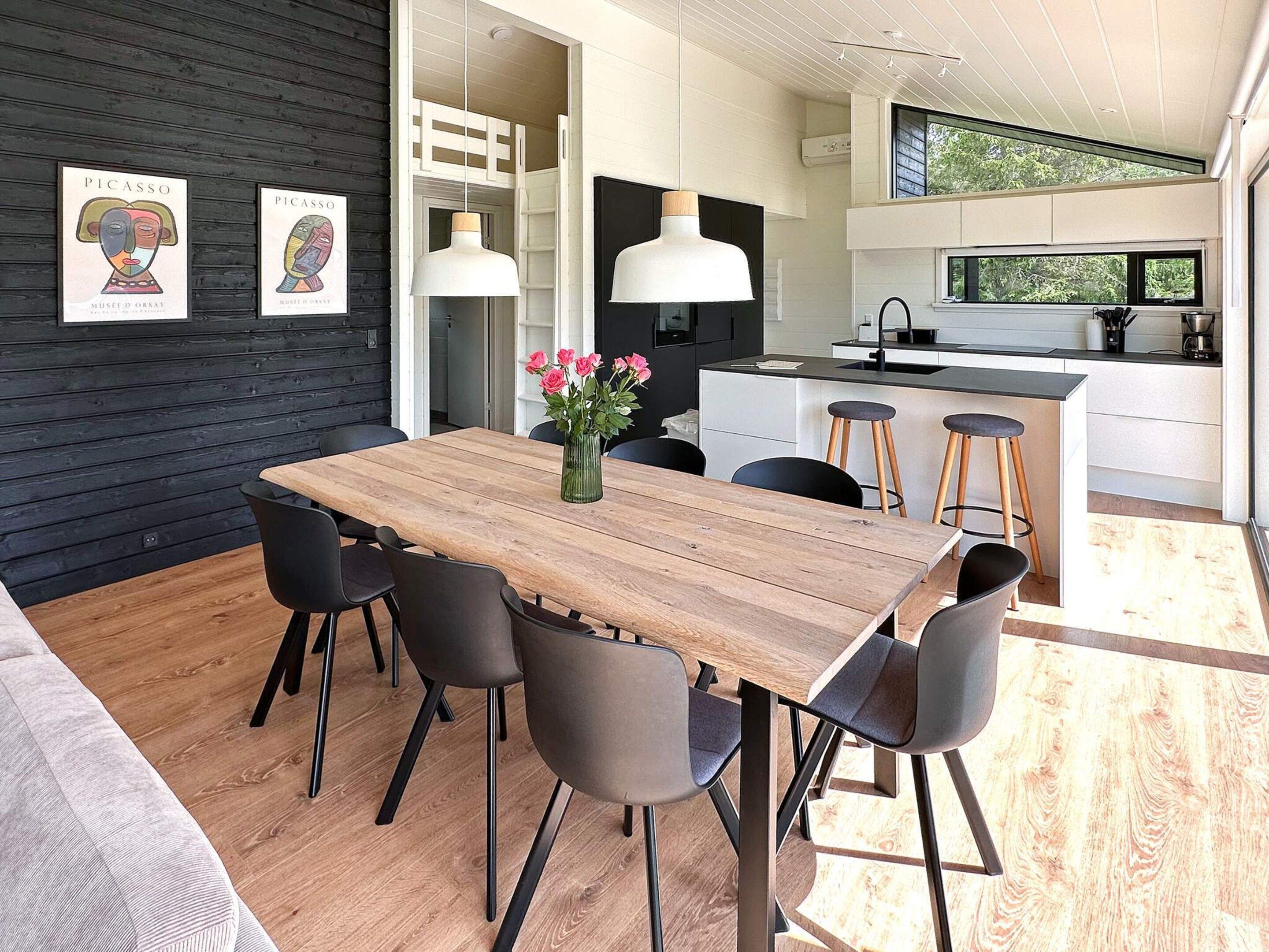 Eine moderne Küche mit einer zentralen Kochinsel, Pendelleuchten und einem Essbereich mit Holztisch und Stühlen.