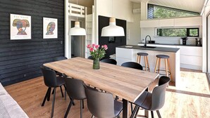 Cocina moderna con isla central, iluminación colgante y comedor con mesa y sillas de madera.