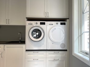 A compact laundry area with two front-loading washing machines, a sink, and a window.