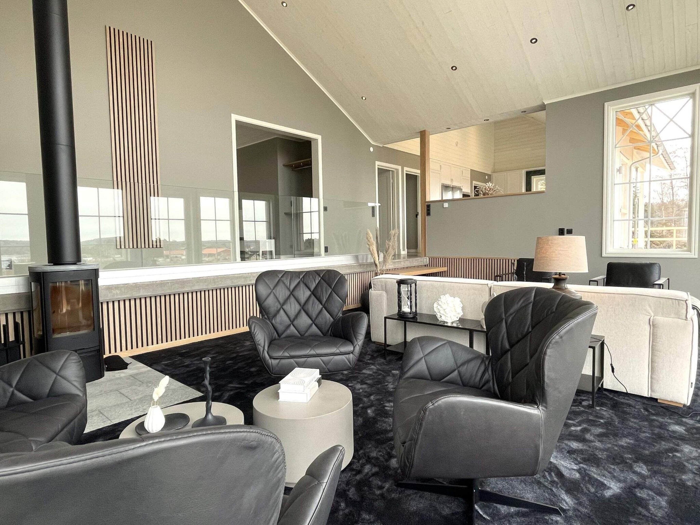 A modern hotel room with leather sofas, a round coffee table, a fireplace, and large windows offering a view.