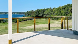Un espacio al aire libre techado con piso de concreto, baranda de madera y vista a un cuerpo de agua y vegetación.