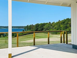 A covered outdoor area with a concrete floor, a wooden railing, and a view of a body of water and greenery. - 5 Star Holiday Home in Uddevalla (Uddevalla)