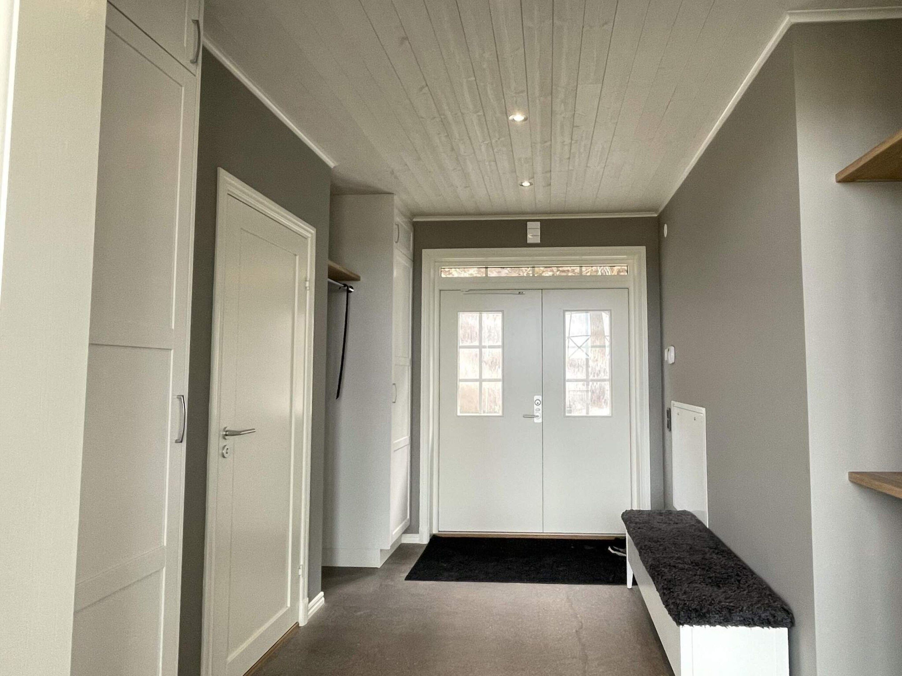 A hallway with a double door, a bench, and a carpeted floor.