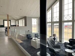 A modern interior with a glass railing, a dining area, and large windows offering a view of the outdoors.